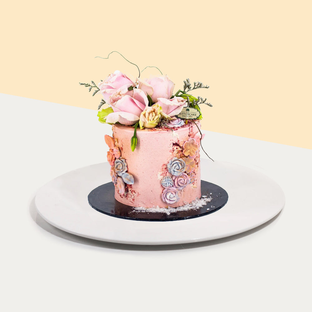 Buttercake coated with pink buttercream, decorated with painted flower swirls and fresh flowers