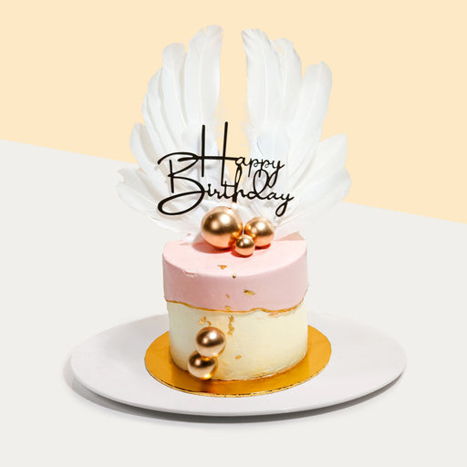 Moist chocolate cake coated with buttercream, adorned with decorative metallic balls and white wings