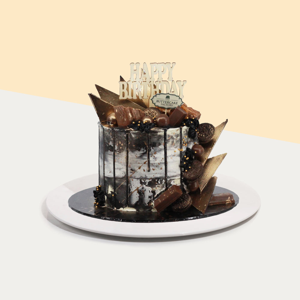 Butter cake coated in black and white marble buttercream, topped with edible gold sprayed candies and chocolate shards