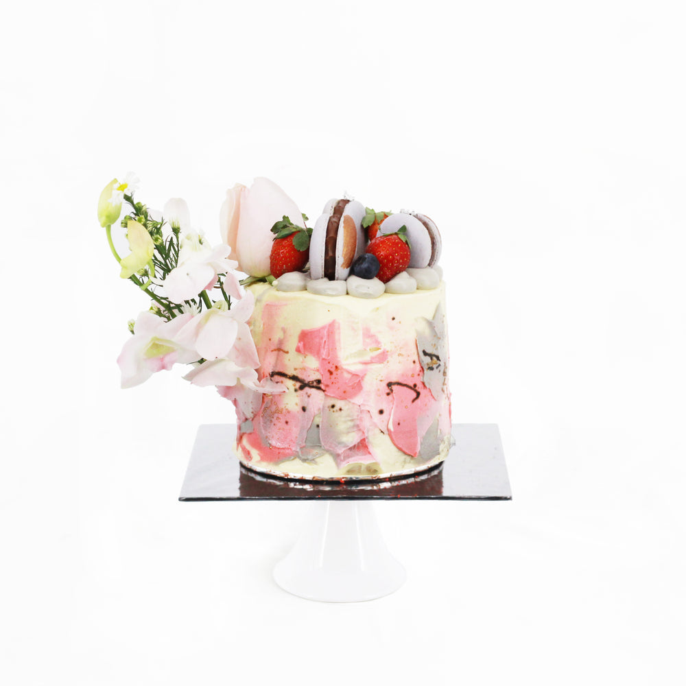 Caramel cake with painted buttercream design, topped with macarons and strawberries