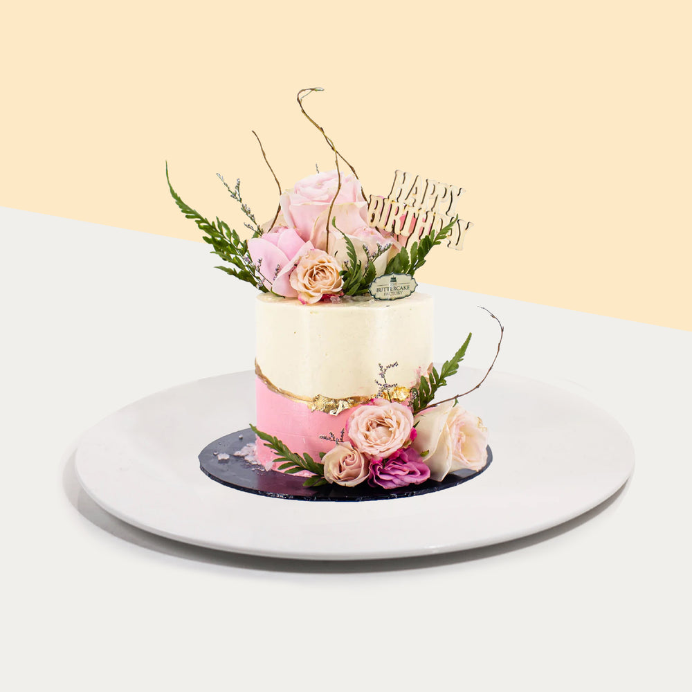 Half pink and white buttercream cake with golden decals, topped with fresh roses