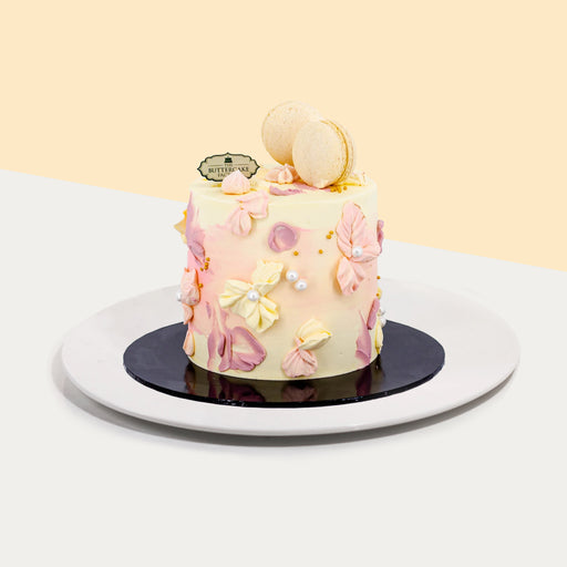 Pastel coloured buttercream cake, with hand piped flower petals and paint strokes, with two macarons on top