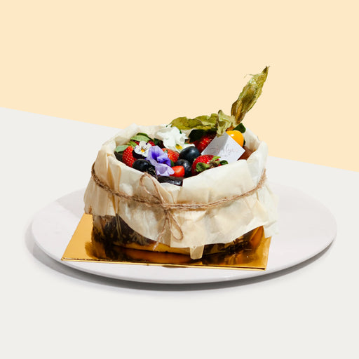 Burnt cheesecake wrapped with parchment paper, adorned with colorful fresh fruits and edible flowers