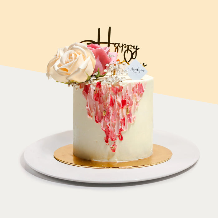 White buttercream cake, with painted strokes of buttercream in pink and red on the side, with faux roses on top