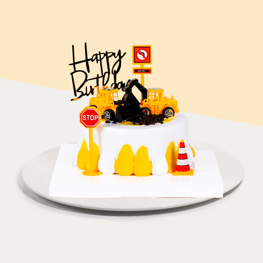 Construction themed cake, with construction vehicles, traffic cones and a stop sign.
