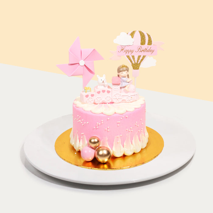 Pink and white buttercream cake, with a girl riding a train cake topper