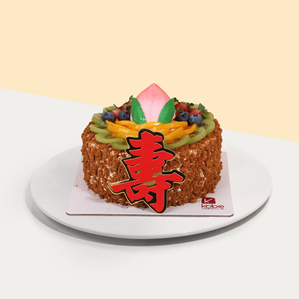 Vanilla chiffon fruit cake, covered in biscuit crumbs with a 寿 cake topper and peach