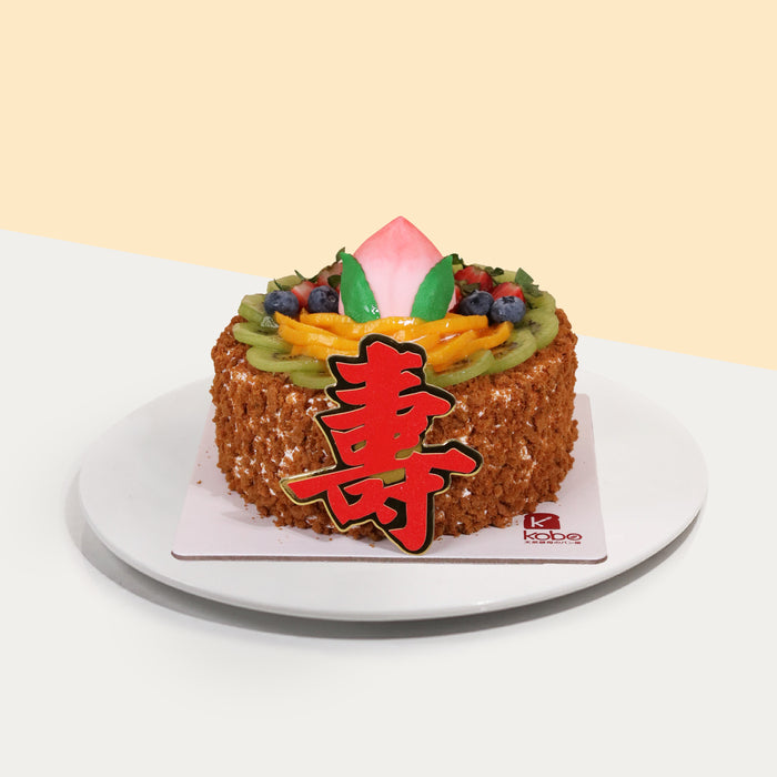 Vanilla chiffon fruit cake, covered in biscuit crumbs with a 寿 cake topper and peach