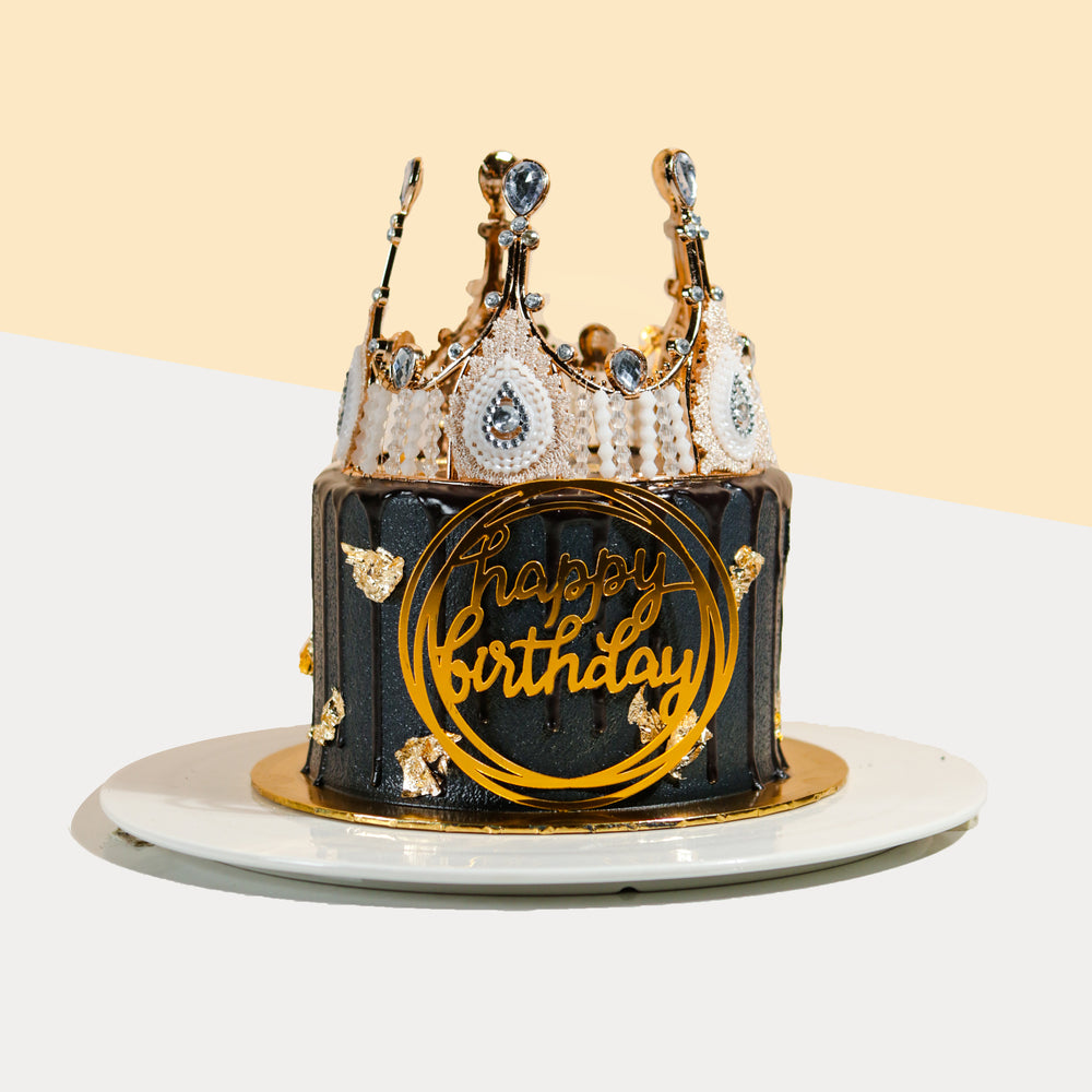 Black buttercream frosted cake with golden Happy Birthday topper, and a crown on top