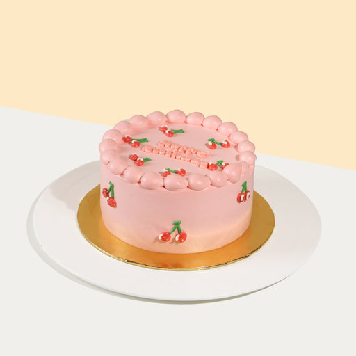 Pink buttercream cake, with piped dollops of cream and hand piped cherries