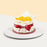 Cake topped with rose shaped mango slices, wrapped in baking paper with ribbon