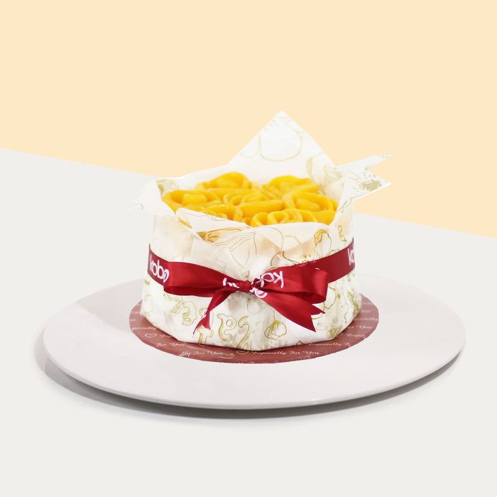Cake topped with rose shaped mango slices, wrapped in baking paper with ribbon