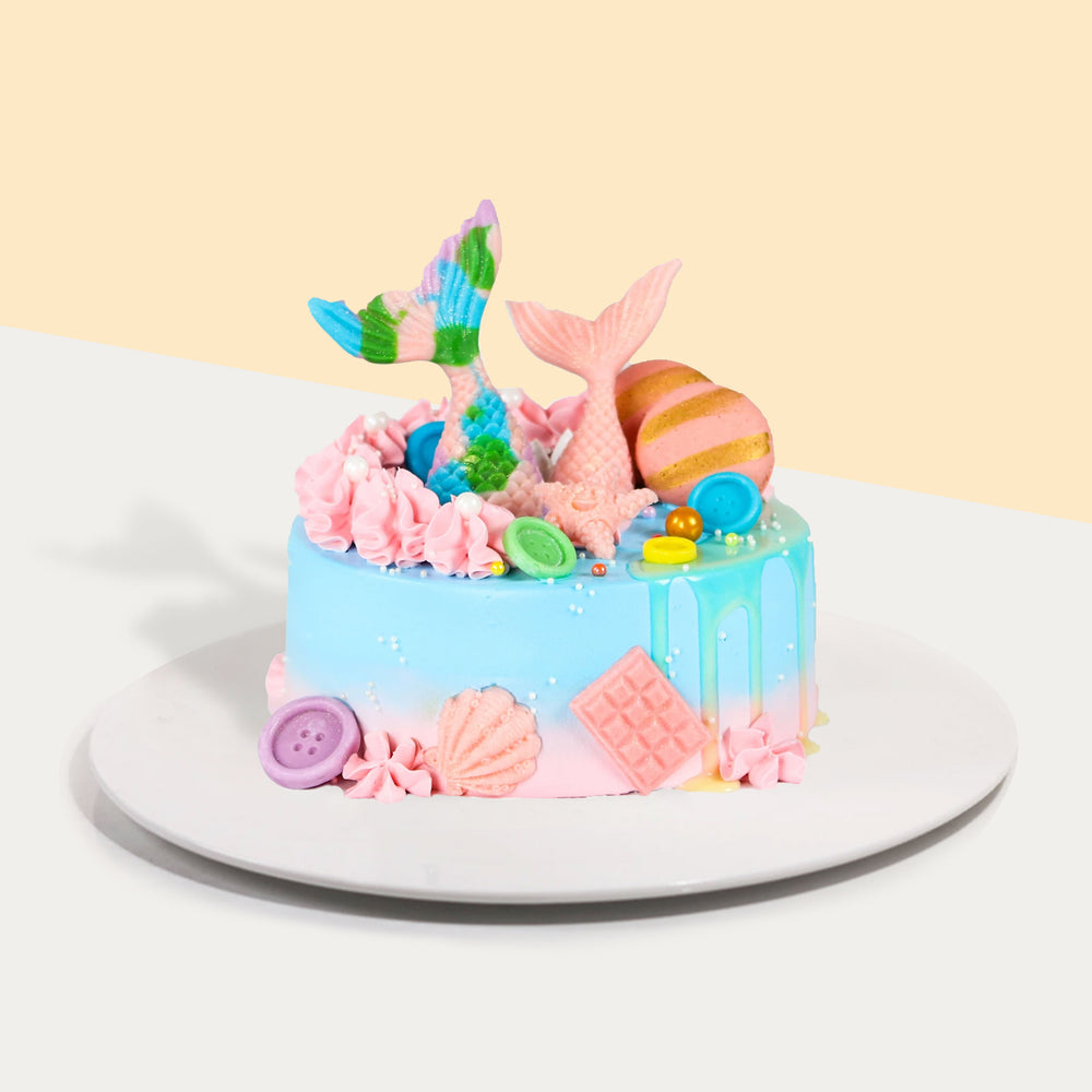 Blue cream cake with white chocolate mermaid decorations and macarons