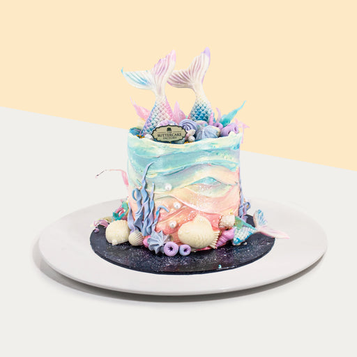 Buttercream cake with mermaid and sea themed decorations, topped with white chocolate mermaid tail, shells and seaweed